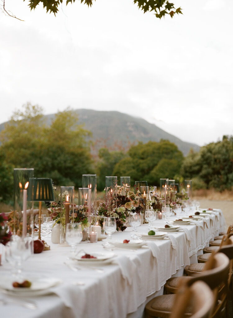  Elegant outdoor wedding reception dinner with long banquet tables, romantic candlelight, and lush floral centerpieces as guests enjoy the evening celebration..